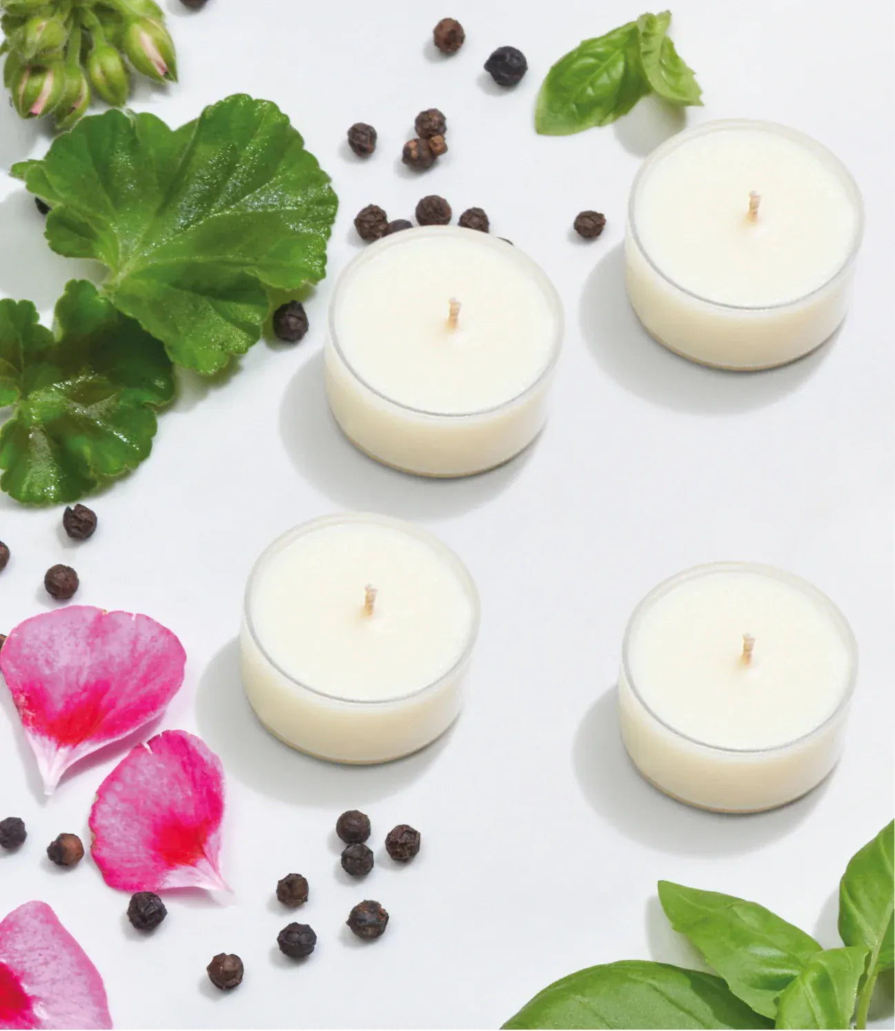 Four Imogen's luxuries Calm tea lights on a light background surrounded by flowers, leaves and peppercorns