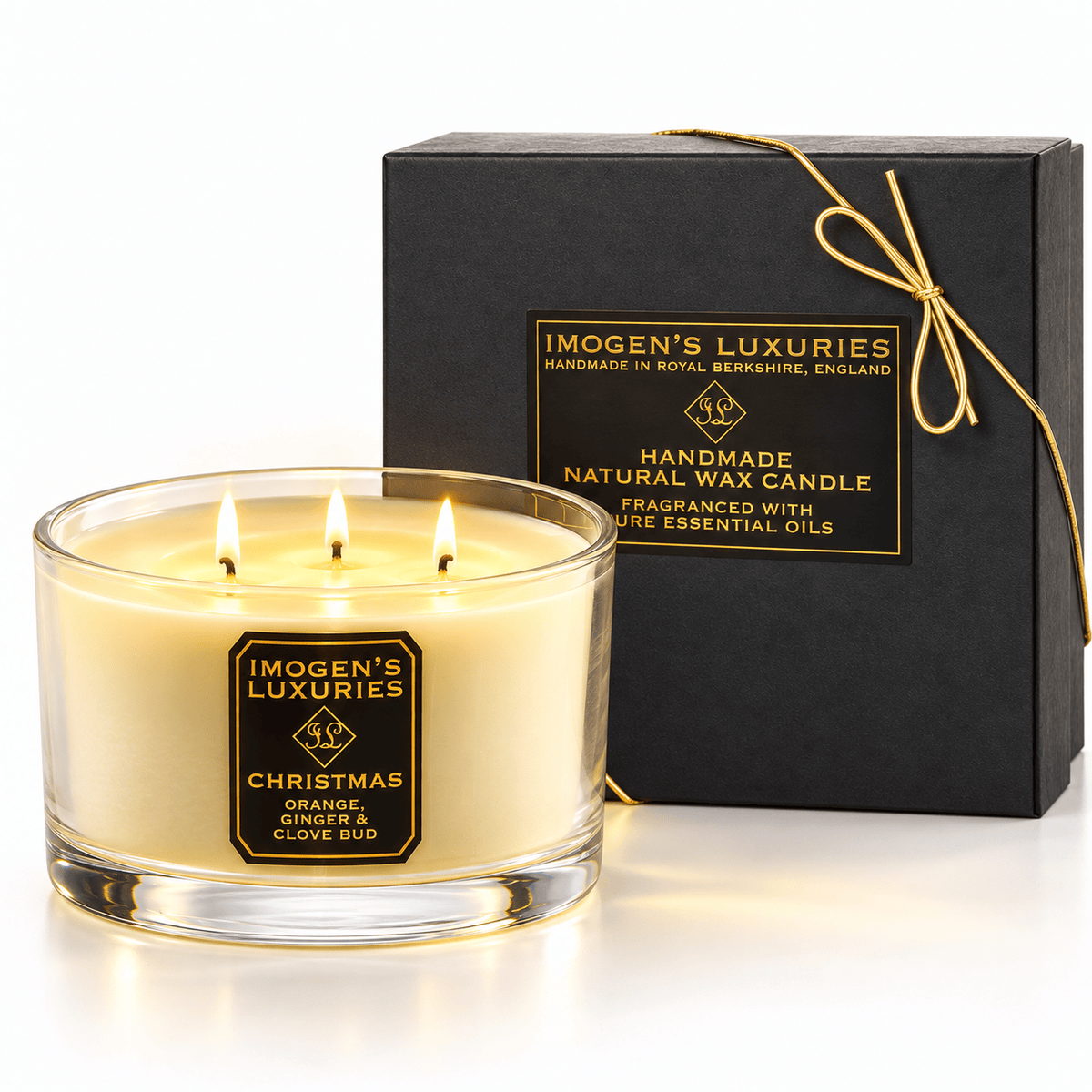 Cream coloured natural wax candle in glass container with 3 wicks which are all lit. Candles is scented with Orange, Cinnamon, Clove and Ginger Essential Oils. On the glass container is a black and gold label saying "Imogen's Luxuries" "Christmas". The candle sits by a solid black and gold box with a black and gold label saying "Handmade Natural Wax Candle fragranced with pure essential oils. There is a fine gold bow across the box.