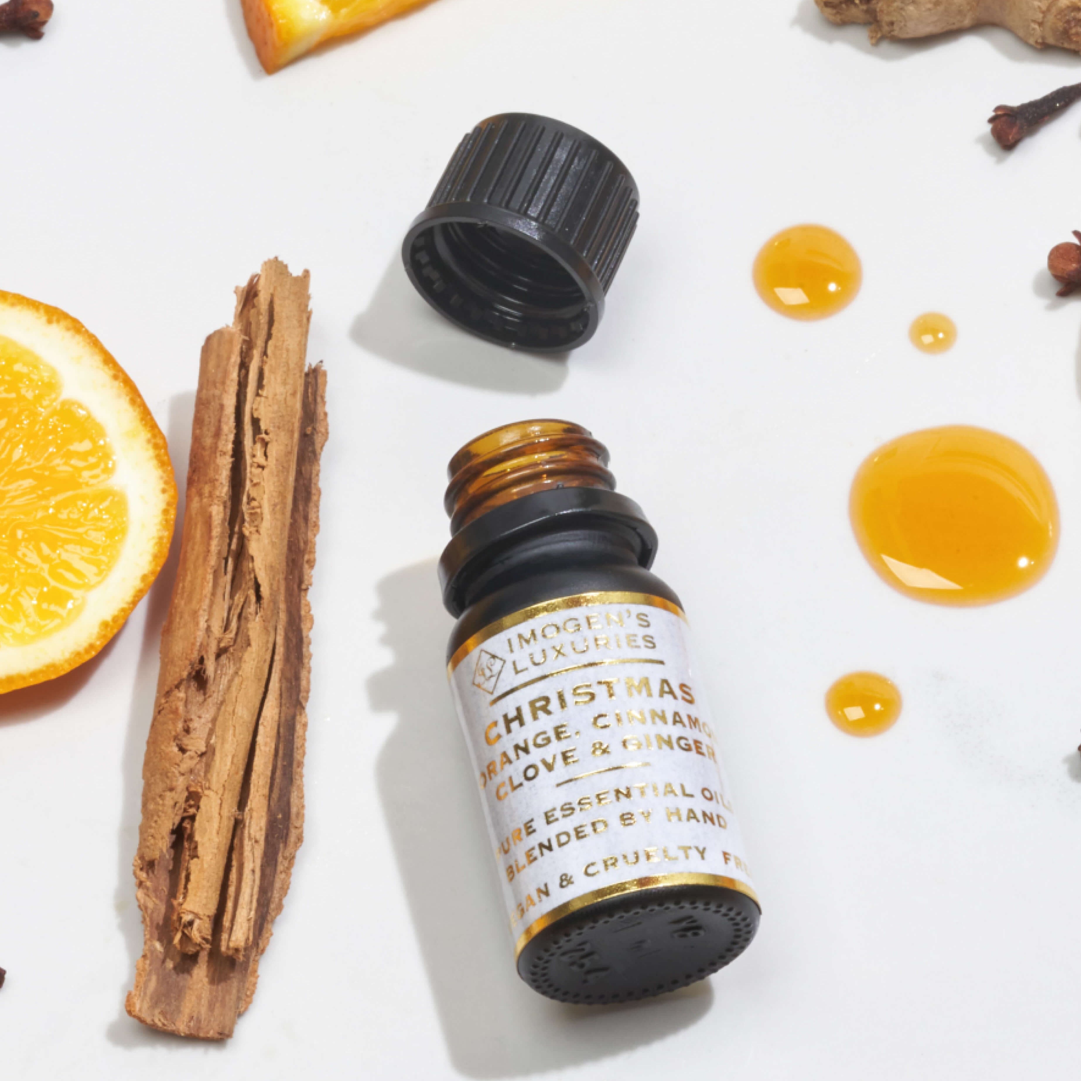 Imogen’s Luxuries Christmas pure essential oil blend. Award-winning, highly concentrated mix of Orange, Cinnamon, Clove and Ginger pure essential oils. All-natural festive scent, shown in a 10ml black dropper bottle surrounded by matching spices and citrus botanicals.