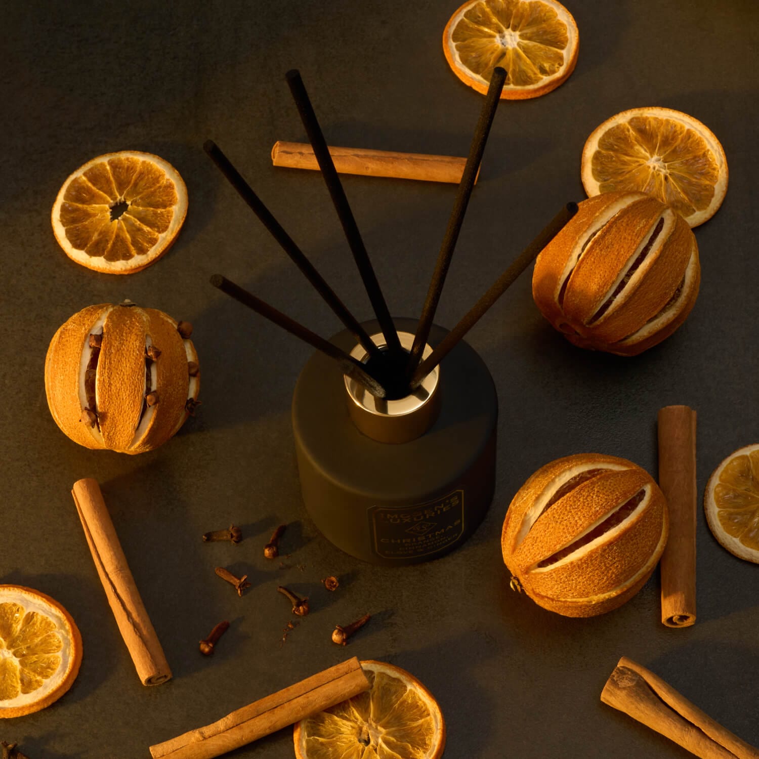 Black Christmas reed diffuser with gold collar scented with Orange, Cinnamon, Clove and Ginger pure essential oils. Diffuser is shown with 6 thick black reed sticks surrounded by cinnamon sticks, clove pieces and orange slices. Handmade in Berkshire by Imogen's Luxuries