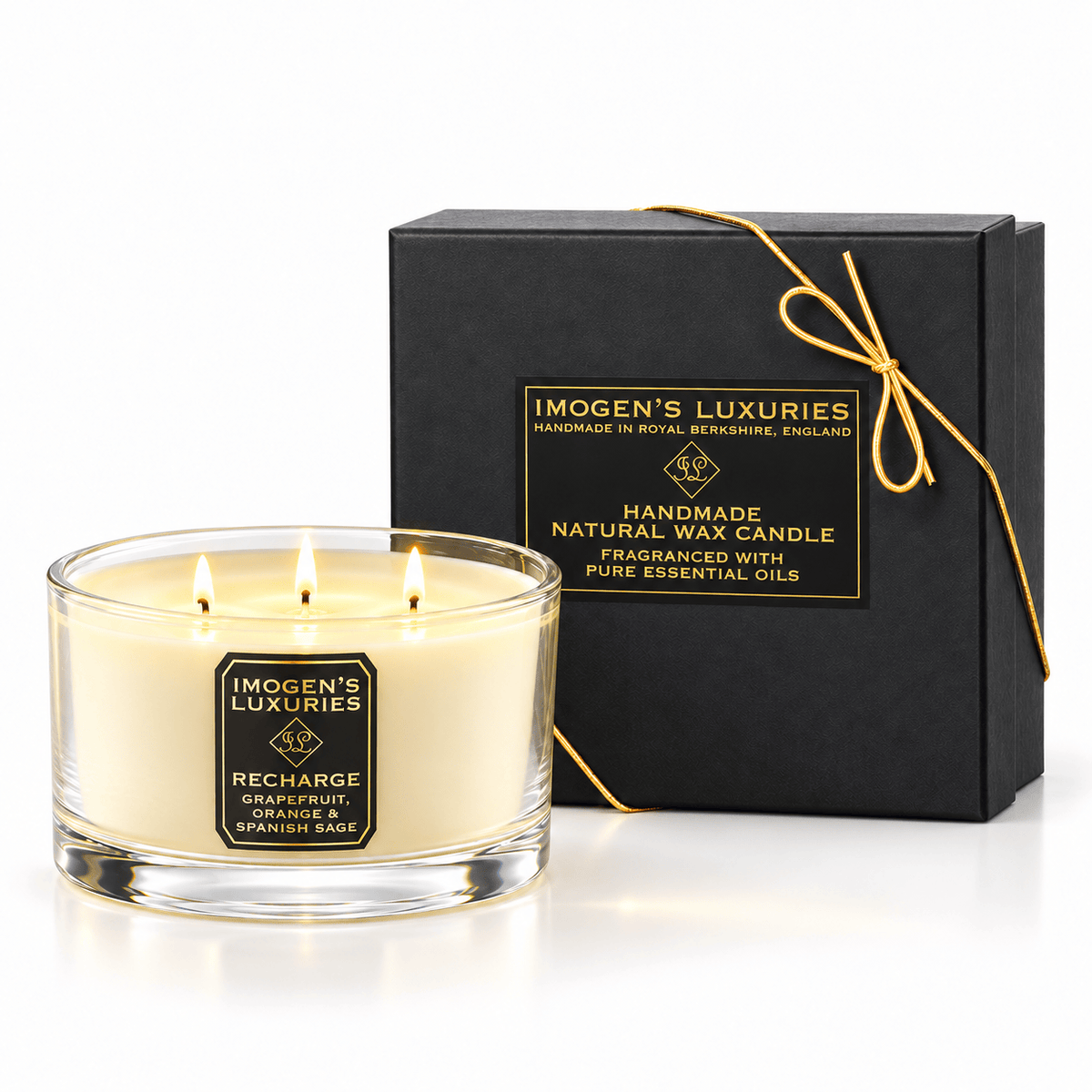 Cream coloured natural wax candle in glass container with 3 wicks which are all lit. Candles is scented with Orange,Grapefruit & Spanish Sage Essential Oils. On the glass container is a black and gold label saying "Imogen's Luxuries" "Recharge". The candle sits by a solid black and gold box with a black and gold label saying "Handmade Natural Wax Candle fragranced with pure essential oils. There is a fine gold bow across the box.