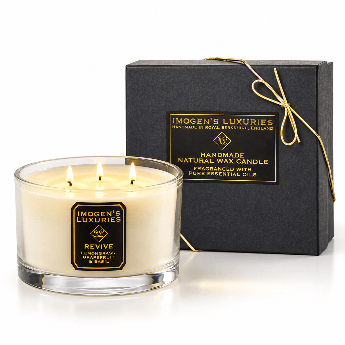 Cream coloured natural wax candle in glass container with 3 wicks which are all lit. Candles is scented with Lemongrass, Grapefruit & Basil Essential Oils. On the glass container is a black and gold label saying "Imogen's Luxuries" "Revive". The candle sits by a solid black and gold box with a black and gold label saying "Handmade Natural Wax Candle fragranced with pure essential oils. There is a fine gold bow across the box.