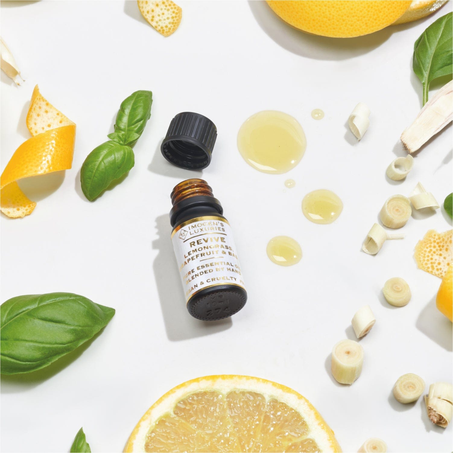 Revive 100% pure essential oil blend of Lemongrass, Grapefruit & Basil in a 10ml black glass bottle. Image shows the bottle with the black lid off with drops of essential oil surrounded by pieces of Lemongrass, slices of Grapefruit and Basil leaves.