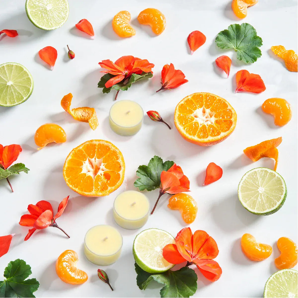 3 Imogen's Luxuries Balance tea lights surrounded by Geranium leaves and flowers, Bergamot slices and segments of Tangerine on a light background.