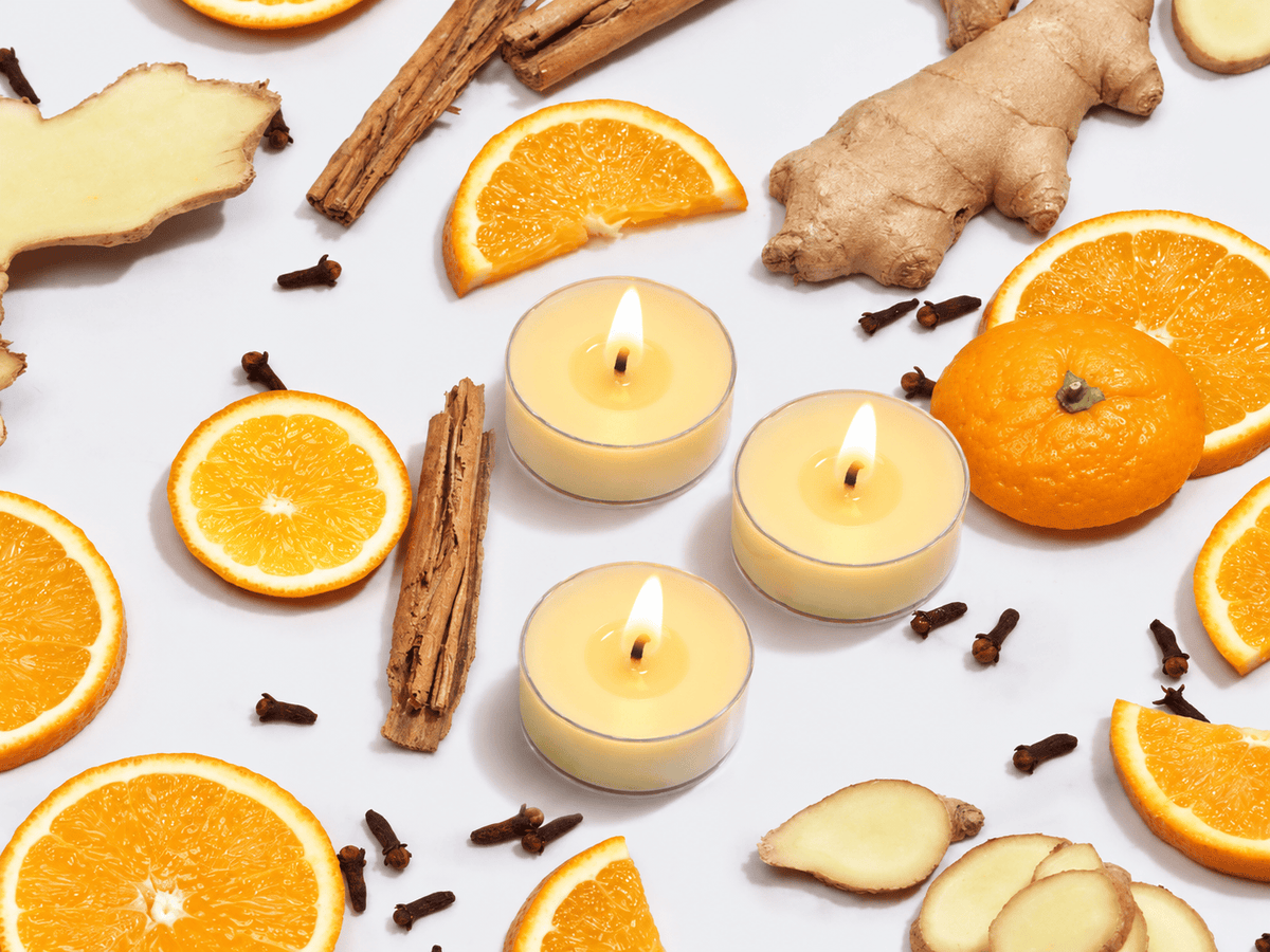 Imogen's Luxuries Christmas tea lights surrounded by orange sliced, cinnamon sticks, cloves and ginger pieces. The 3 tea-light candles are shown in polycarbonate cups and are lit
