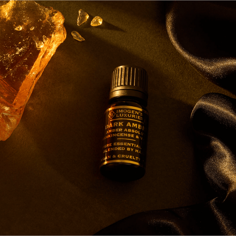 10ml black dropper bottle of Imogen’s Luxuries Dark Amber Arabian Oud oil blend. Notes of Amber Absolute, Vetiver and Frankincense beside a large piece of Amber resin on a dark silk surface. All Natural Essential Oils. Vegan and Cruelty Free.