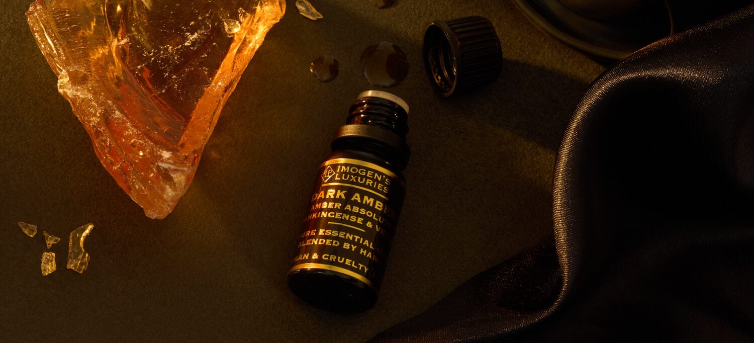 10ml black bottle of Imogen’s Luxuries Dark Amber Oud Oil blend with notes of Amber Absolute, Vetiver and Frankincense. Bottle is beside a piece of Amber resin on a dark background.