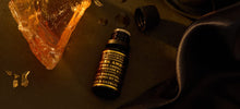 10ml black bottle of Imogen’s Luxuries Dark Amber Oud Oil blend with notes of Amber Absolute, Vetiver and Frankincense. Bottle is beside a piece of Amber resin on a dark background.