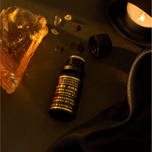 10ml Black dropper bottle of Imogen's Luxuries Dark Amber Oud Oil Blend. Notes of Amber Absolute, Vetiver and Frankinsence. Bottle is beside Amber resin on a dark background with an oil burner.