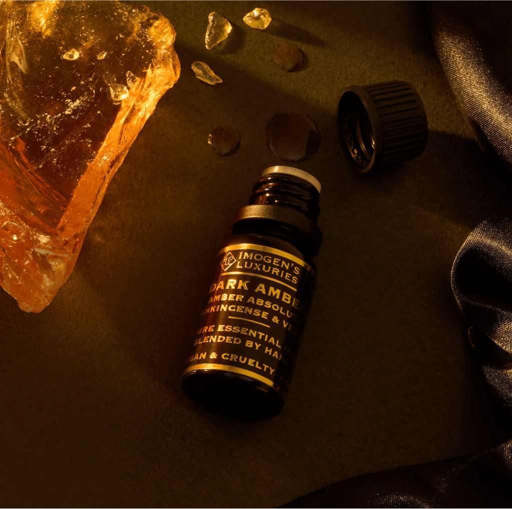 10ml black bottle of Luxury Dark Amber Oud Oil. Blend of Amber Absolute, Vetiver and Frankincense. Bottle is beside Amber Resin. All Natural and alcohol free.