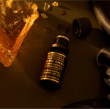 10ml black bottle of Luxury Dark Amber Oud Oil. Blend of Amber Absolute, Vetiver and Frankincense. Bottle is beside Amber Resin. All Natural and alcohol free.