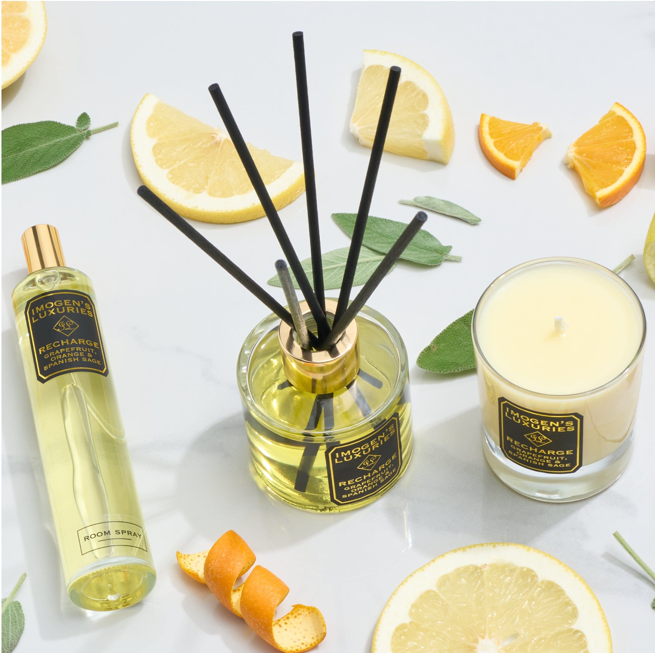 Aromatherapy candle, reed diffuser and room spray scented with pure essential oils of Grapefruit, Orange and Spanish Sage. Products are on a light background surrounded by pieces of orange and grapefruit with Sage leaves