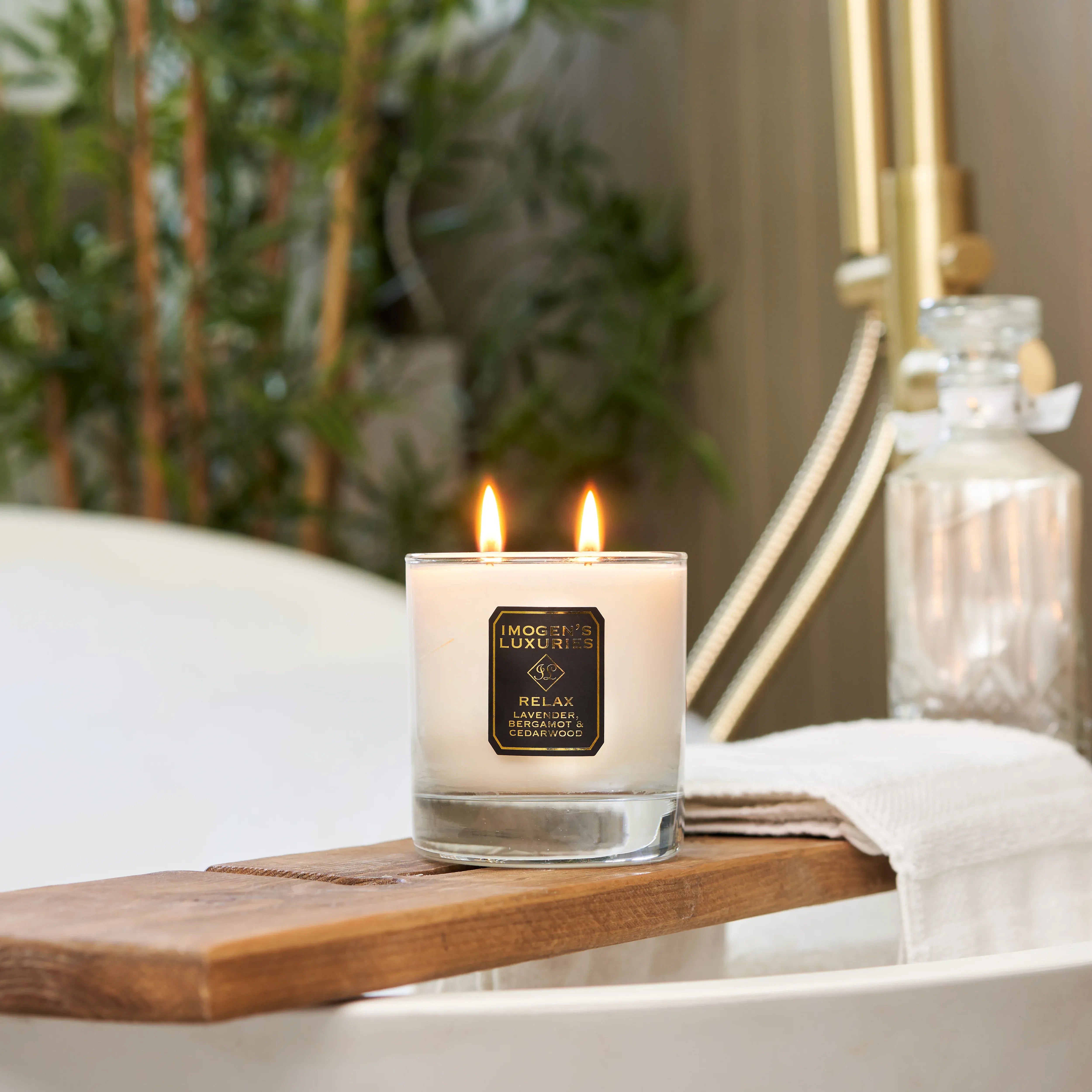 Luxury Imogen’s Luxuries Relax natural wax scented candle with lavender, bergamot and cedarwood essential oils. The double wick glass jar candle is styled on a wooden bath tray in a spa bathroom setting.