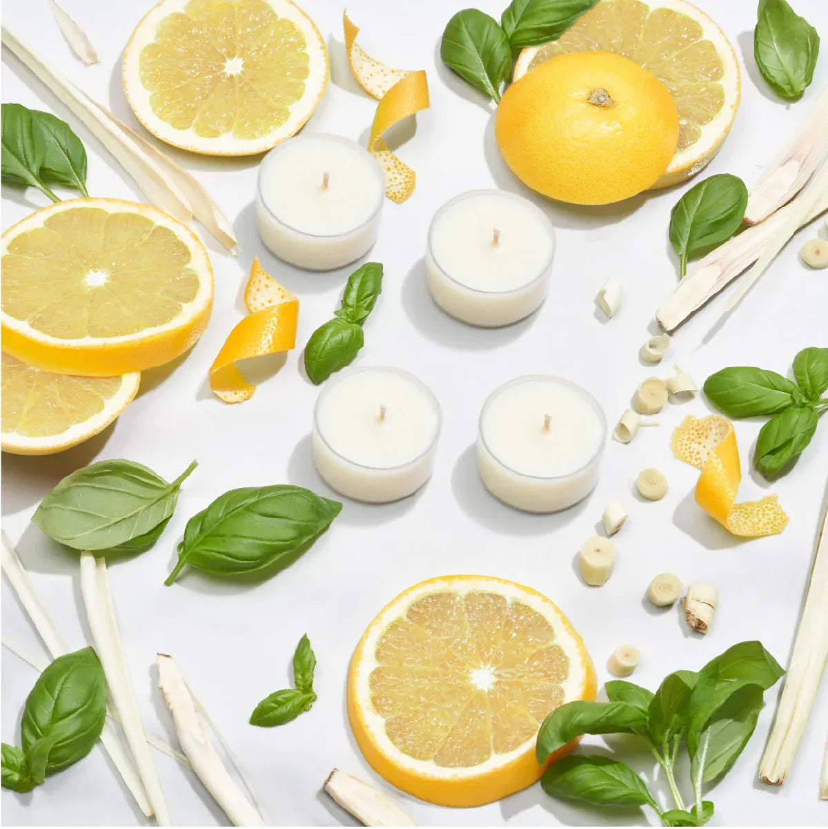 Four Imogen's Luxuries Revive scented tea-light candles surrounded by grapefruit slices, strips of lemongrass and fresh basil leaves