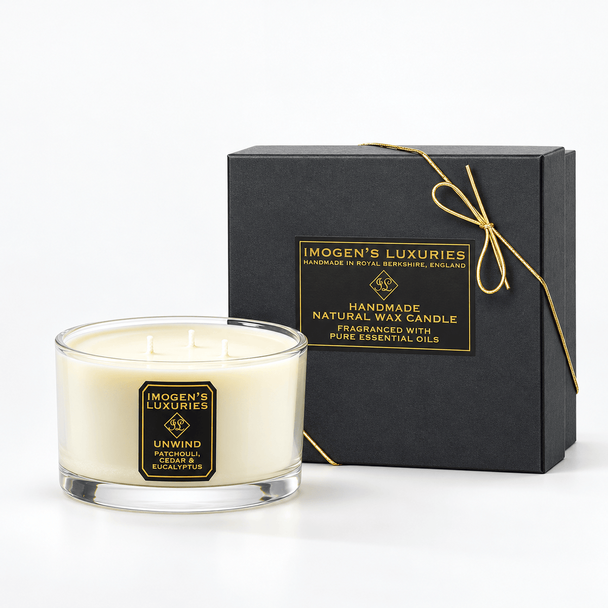 Cream coloured natural wax candle in glass container with 3 wicks. Candles is scented with Patchouli, Cedarwood & Eucalyptus Essential Oils. On the glass container is a black and gold label saying "Imogen's Luxuries" "Unwind". The candle sits by a solid black and gold box with a black and gold label saying "Handmade Natural Wax Candle fragranced with pure essential oils. There is a fine gold bow across the box.