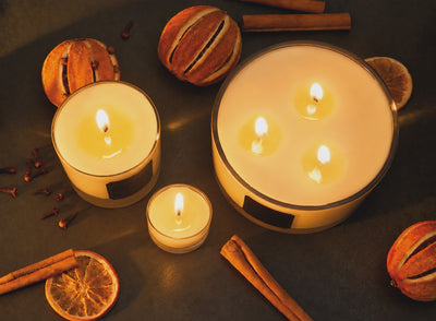 Multiple christmas candles by Imogen's Luxuries burning with a flickering flame. Image includes a 1 wick candle, a 3 wick candle and a tea light. All are made with Soy wax and scented with Orange, Cinnamo, Clove and Ginger essential oils