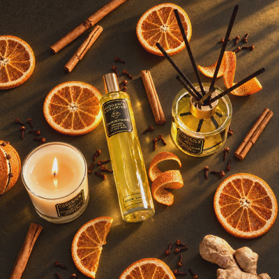 Christmas collection from Imogen's Luxuries all scented with Orange, Cinnamon, Clove and Ginger essential oils. Available in 1 wick candle which is shown lit with a flickering flame, reed diffusers and room sprays. The products are surrounded by dried oranges, cinnamon sticks and cloves. The image is set on a dark background