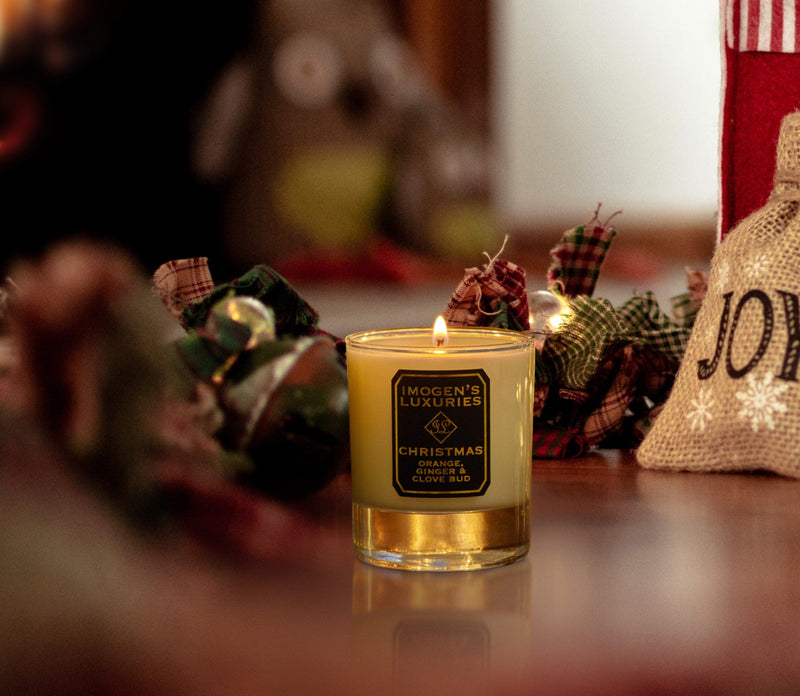 Imogen's Luxuries luxury Christmas scented candle. Fragranced with our award-winning natural blend of Orange, Cinnamon, Clove and Ginger Essential Oils. Beautiful lit candle is displayed on a festive table with presents and a Christmas garland.